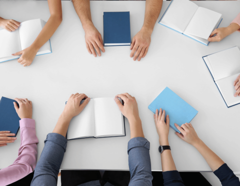 Image of table with group of people's arms and books visible from the top