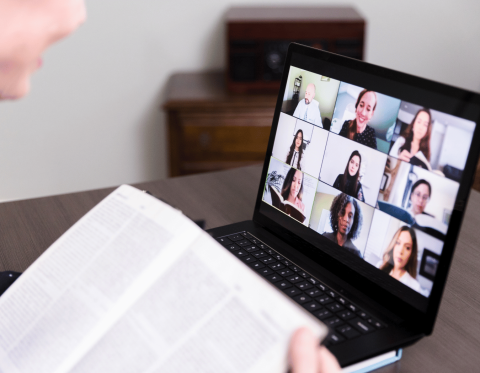 Image of a computer screen with faces and person off-screen holding a book