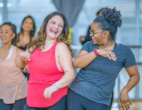 Two women bumping hips at the front of a group dance class