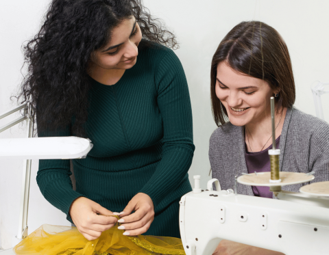 Woman demonstrating technique to a student in front of a sewing machine