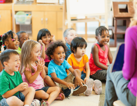 Group of young children listening to adult reading them a picture book