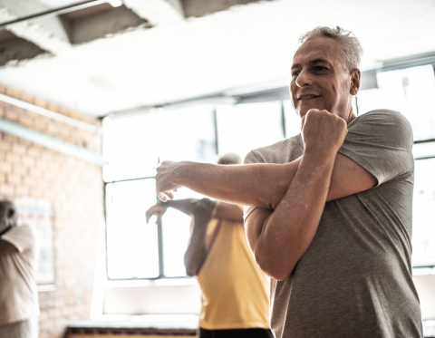 Older adults in a fitness class stretching arms across torsos