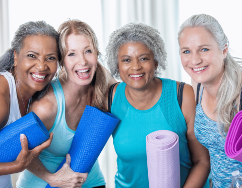 Group of four women standing together with rolled yoga mats