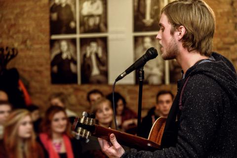 man with long hair at microphone singing with guitar to audience