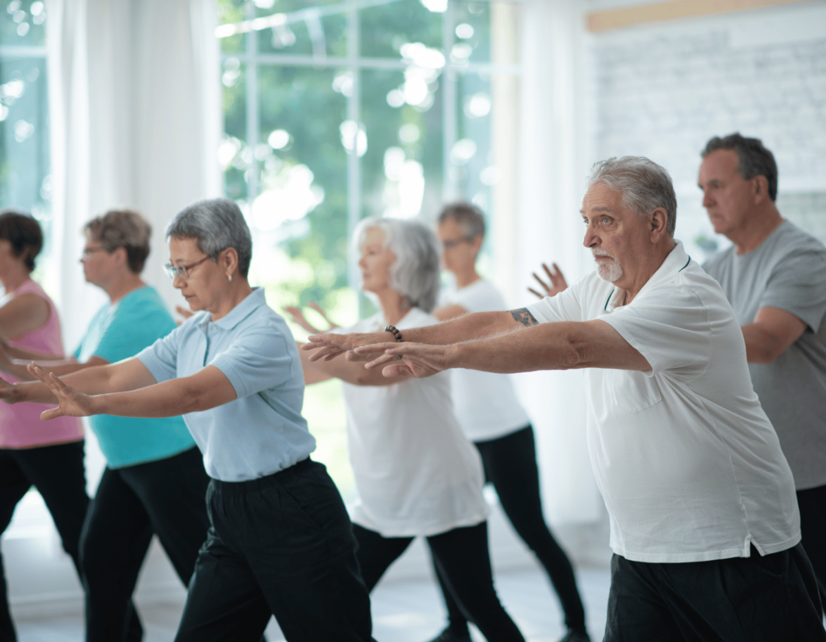 Group of older adults in standing poses being led in Tai Chi motions