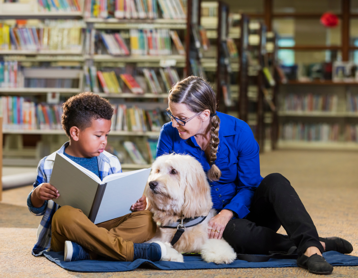 Child and adult reading a book to a dog